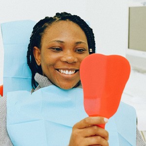 Smiling female patient looking in dental mirror