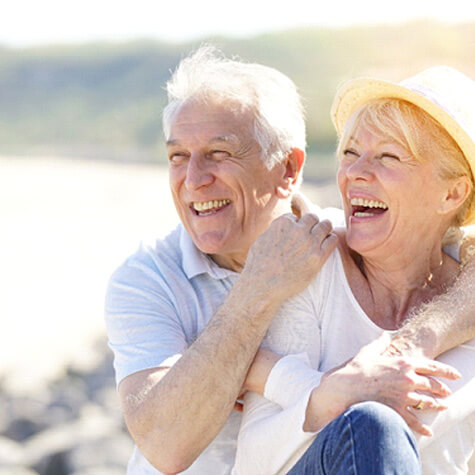 senior couple sitting on a beach and smiling