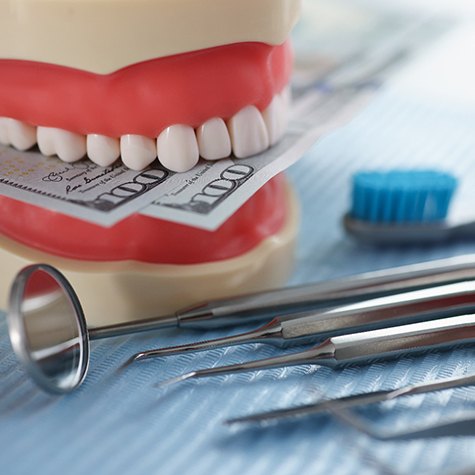 An artificial jaw mockup biting dollar bills while sitting next to dental tools