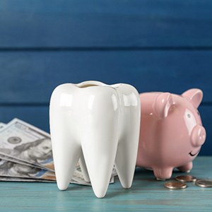 A large ceramic tooth sitting next to a piggy bank and dollar bills