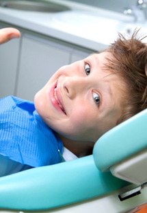 young child giving thumbs up while sitting in dental chair 