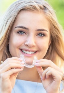 woman smiling while holding clear aligner