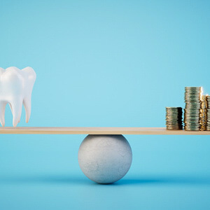 tooth and pile of coins balancing on plank