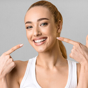 Woman with blond ponytail pointing to her smile